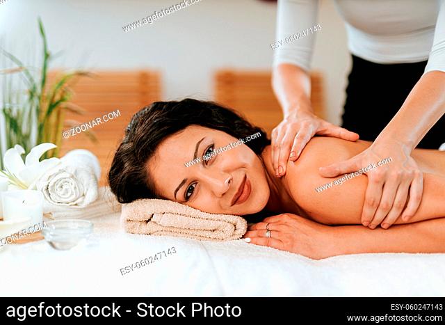 Beauty treatment concept with masseur and her patient. Masseur doing massage on woman body in the spa salon. Beautiful girl with brown curly hair and creol skin...