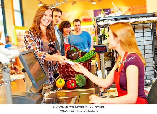 Lächelnde Frau bezahlt Einkauf mit Geldschein bei der Kassiererin im Supermarkt