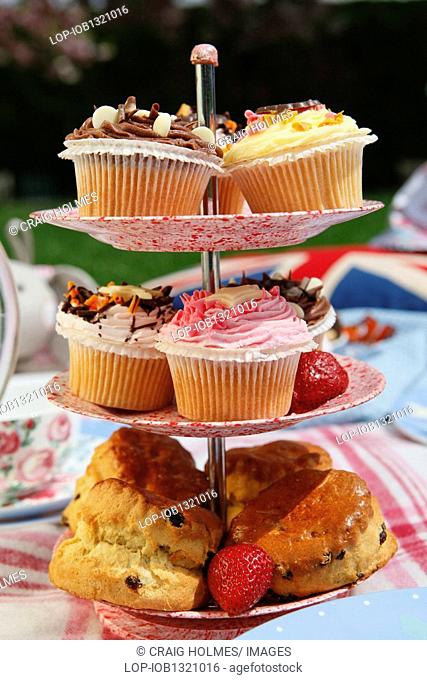 England, West Midlands, Edgbaston, Cup cakes and scones on a cake stand in the centre of a picnic table in the Botanical Gardens in Edgbaston, Birmingham
