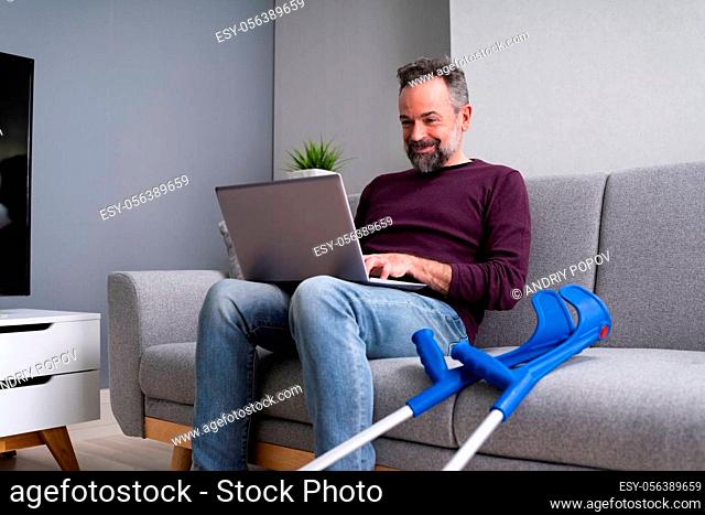 Injured Man With Broken Leg And Crutches Using Laptop
