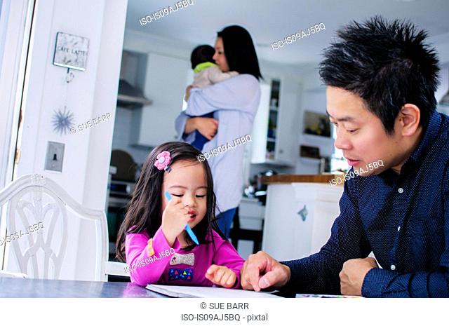 Mid adult father teaching toddler daughter in kitchen
