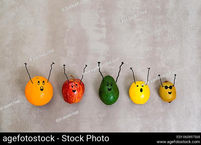 Great concept of healthy eating, diverse fruits with happy faces and arms upwards in gray background, polished concrete. Orange, apple, kiwi, lemon