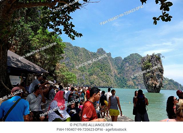 06 March 2019, Thailand, Khao Phing Kan: Tourists walk on the beach of the island Khao Phing Kan in front of the prominent rock Khao Ta-Pu