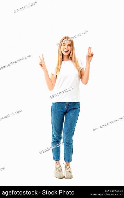 Full length portrait of a happy young woman standing and showing peace gesture with two hands isolated over white background