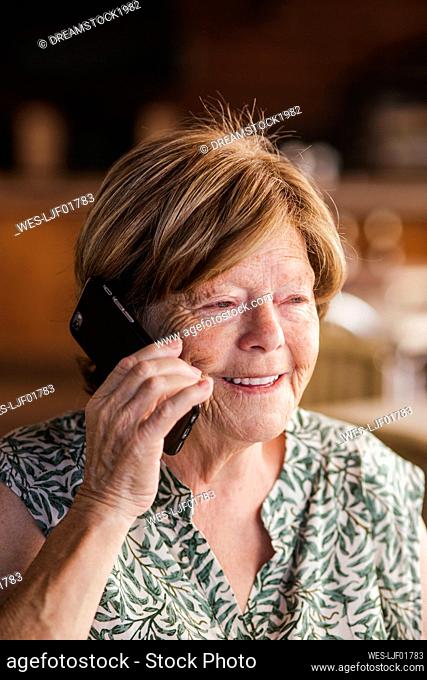 Senior woman smiling while talking on mobile phone at cafe