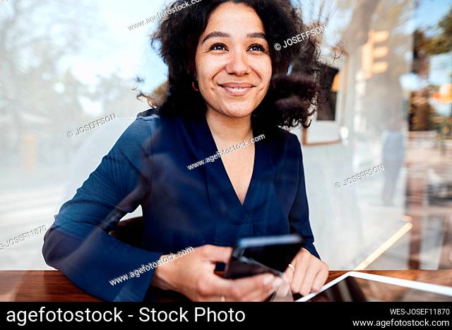 Happy woman with smart phone at table seen through glass