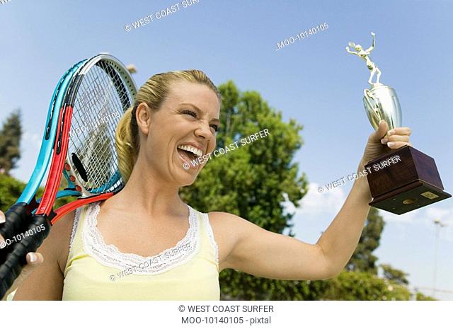 Woman celebrating on tennis court with Tennis Rackets and Trophy