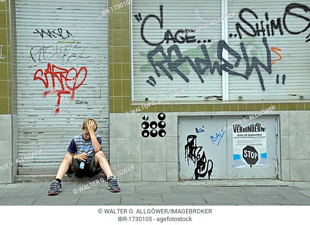 Lonely nine year old boy in front of a closed business which is smeared with graffiti, Germany, Europe