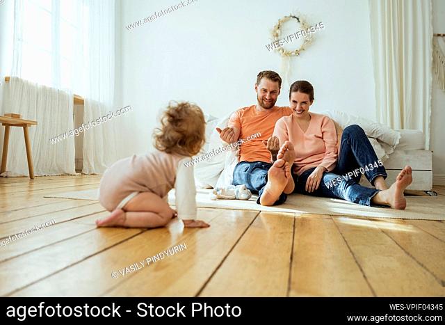 Smiling parents calling daughter crawling at home