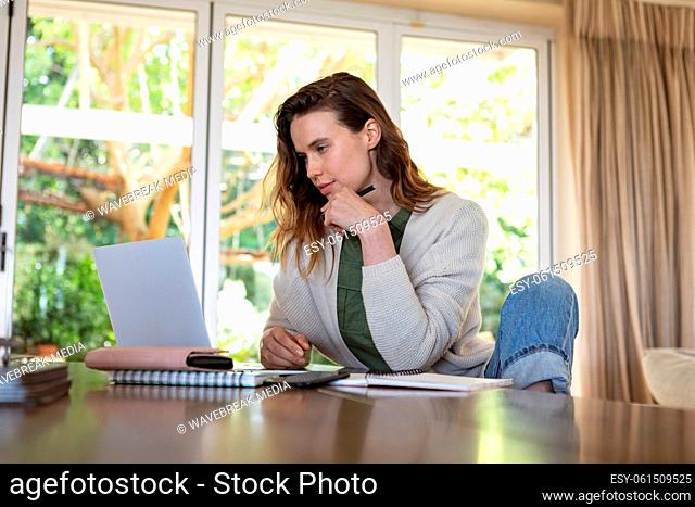 Woman taking notes while using laptop at home