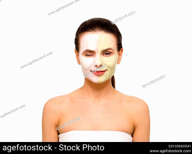 Beauty concept. Isolated on white beautiful woman with facial cream white - green mask on face wink to camera