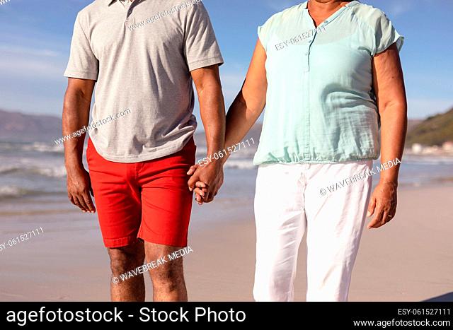 Mid section of african american couple holding hands standing on the beach
