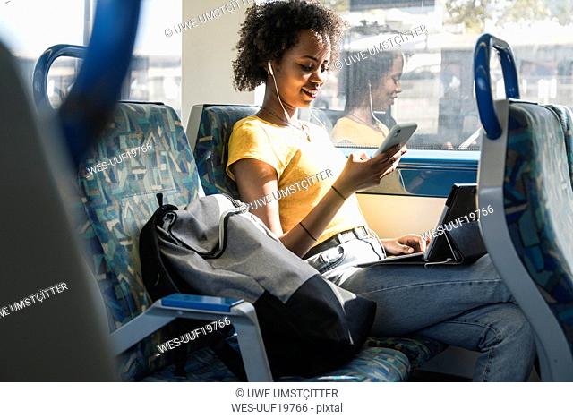 Young woman with earphones using smartphone and tablet on a train