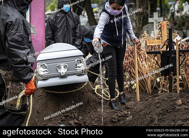 24 June 2020, Mexico, Mexiko-Stadt: A woman wearing a face mask pours holy water into a grave during the funeral of a Covid 19 death victim at the San Isidro...
