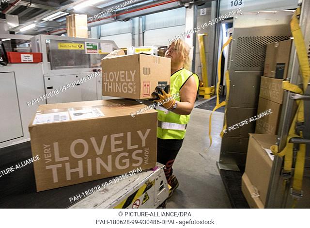 28 June 2018, Germany, Obertshausen: Employee Anna-Maria Tramontana lifts newly arrived parcels onto one of the conveyor belts at the Deutsche Post parcel...