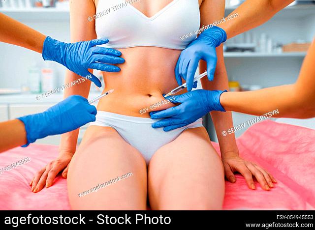 Cosmetician hands in gloves gives botox injection in the stomach to female patient on treatment table. Rejuvenation procedure in beautician salon