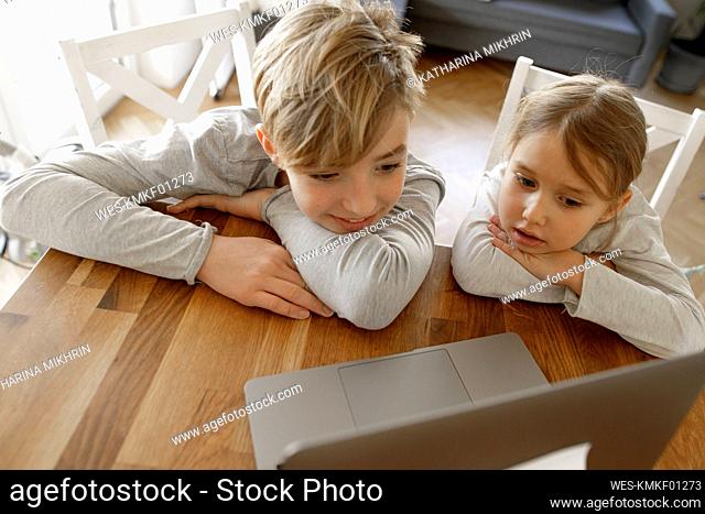 Brother and sister looking at laptop together at home