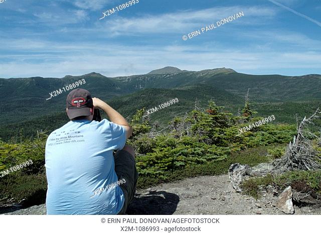 A hiker photographs Mount Washington from Mount Isolation during the summer months in the scenic landscape of the White Mountains