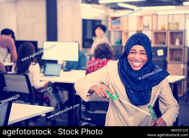 young african american muslim female software developer having fun while making soap bubbles at modern startup office