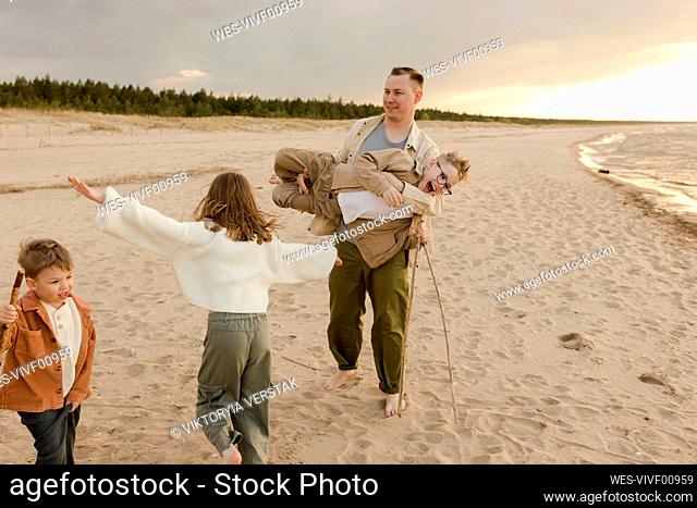 Father having fun with daughter and sons at beach