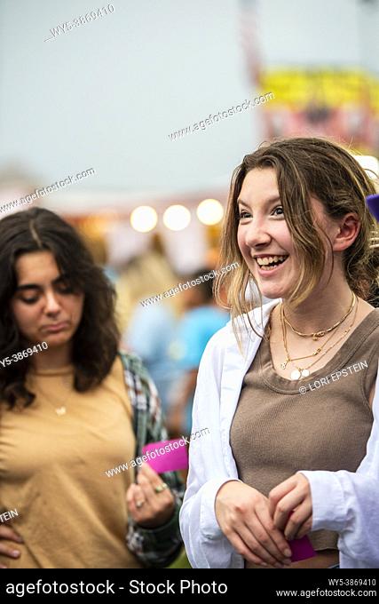 A caucasian teenage girl smiles and laughs with her friends at the county fair in Arlington, Virginia