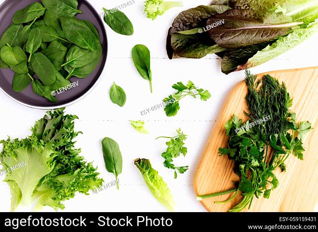 Flat lay with cutting board and bowl of fresh green salad leaves of spinach and lettuce, romaine and parsley, basil on white background