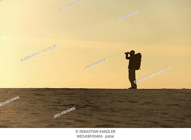 Man with backpack drinking at the beach in the evening light
