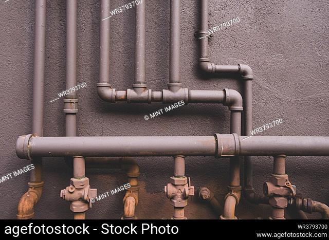 Natural gas utility pipes running along a brown wall, valves and joints