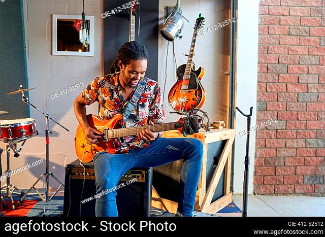 Male musician playing electric guitar in garage recording studio