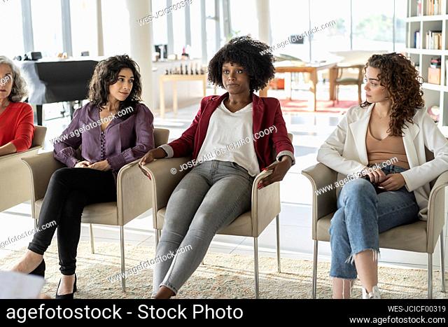 Businesswomen looking at colleague with Afro hairstyle sitting on chair in office