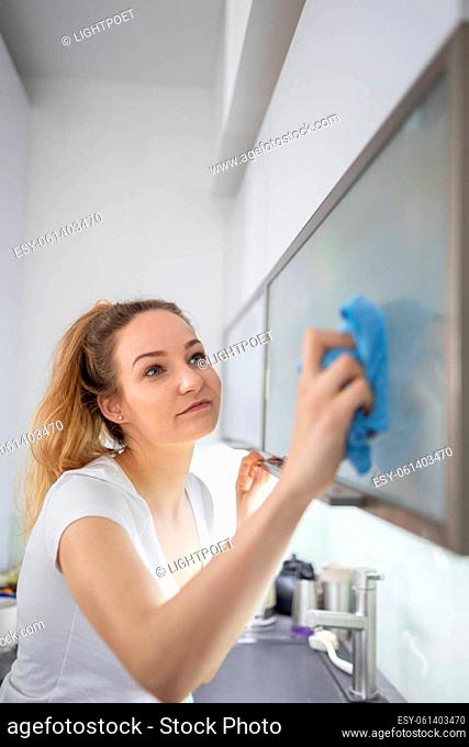 Young woman polishes a modern bright kitchen