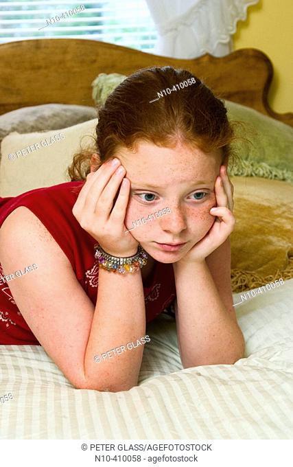 Preteen redhead girl, in Connecticut, USA, reclining on her mother's bed, thinking