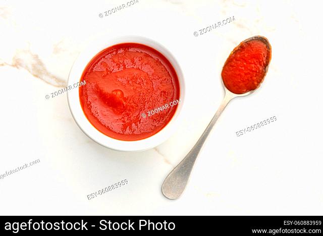 Fresh tomato sauce on bowl and spoon on white marble table. Top view