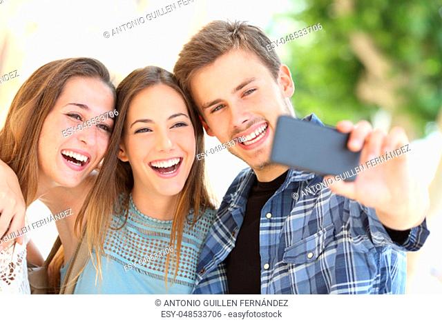 Portrait of three happy friends taking selfies together with a smart phone in the street