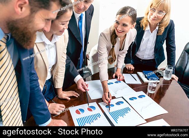 Multi-ethnic team of five dedicated specialists smiling while analyzing various charts with positive statistics about the profit and the development of the...