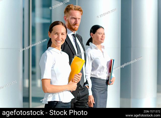 Three businesspeople welcoming you. Woman in white shirt with yellow folder smiling isolated on her collegues