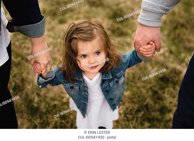 Mother and father holding young daughter's hands, outdoors, elevated view