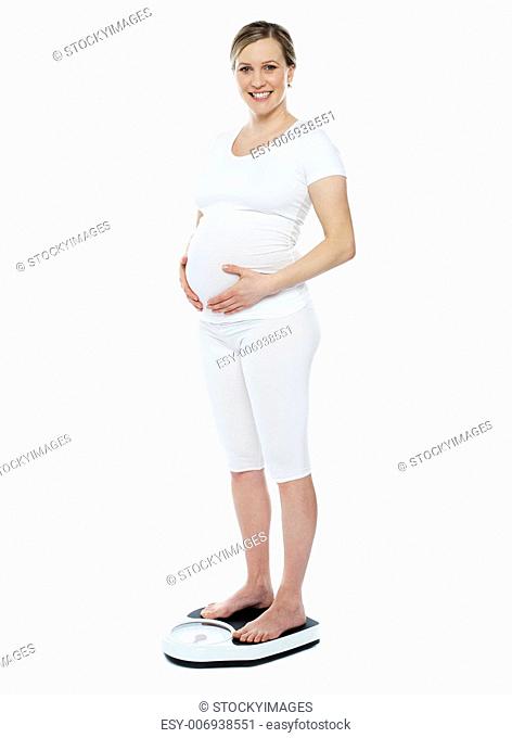 Pregnant woman measuring her weight through weighing scale. Hands on stomach