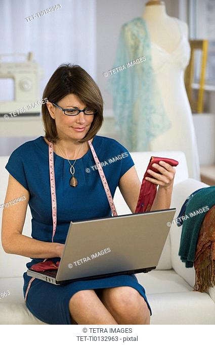 Clothing designer holding fabric and using laptop