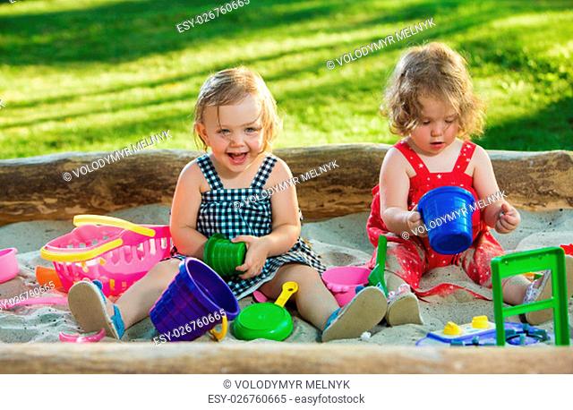 The two little baby girls two-year old playing toys in sand against green grass