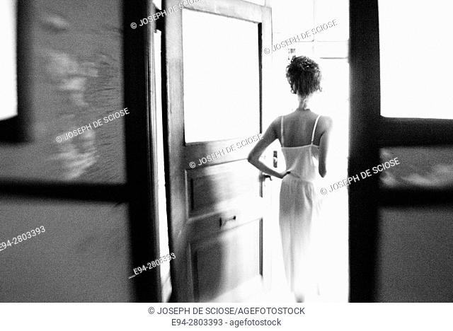 Back view silhouette of a 25 year old woman wearing a white dress walking through a doorway in an abandoned office building