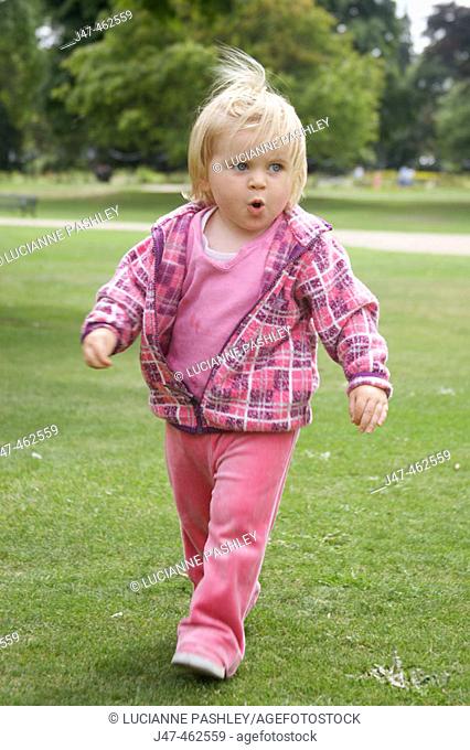 1 year old girl striding through the park