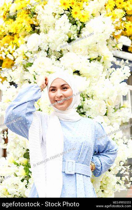 Smiling woman with hand on hip standing in front of white flowers