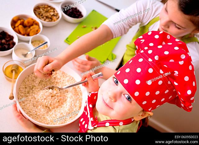 Happy sisters cooking together. Young happy children kids family having fun preparing granola in kitchen at home