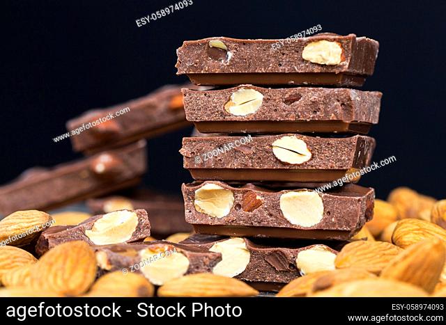 large pieces of chocolate with roasted almond kernels on a wooden table, close-up of natural cocoa products and nuts