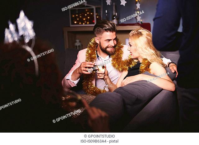 Man and woman at party, sitting on sofa, holding drinks, making a toast