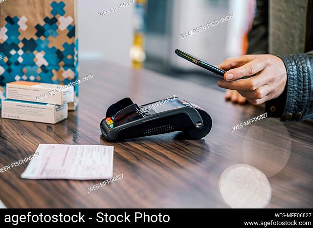 Hand of customer with smart phone at checkout counter in chemist shop