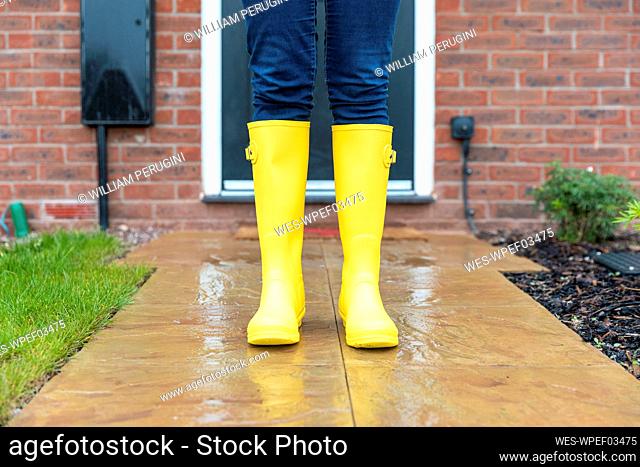 Woman wearing rubber boot standing in back yard during rainy season
