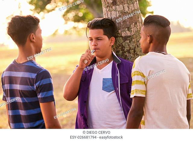 Youth culture, young people, group of male friends, multi-ethnic teens outdoors, multiracial boys together in park. Kids smoking electronic cigarette