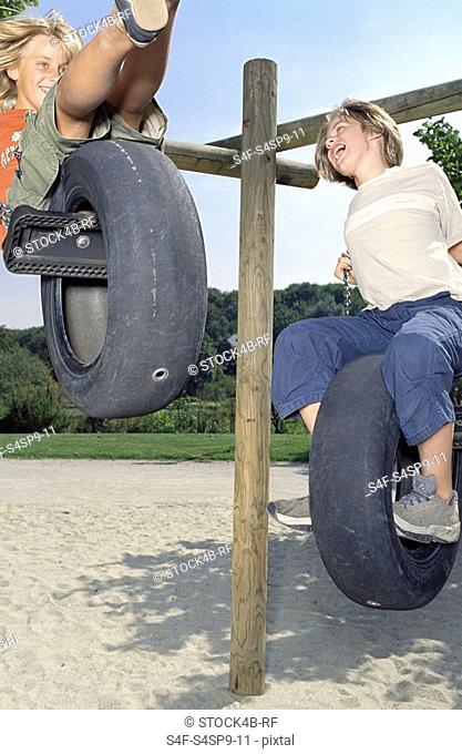 Two Boys playing on a Tire-Swing - Fun - Leisure Time - Playground - Friendship